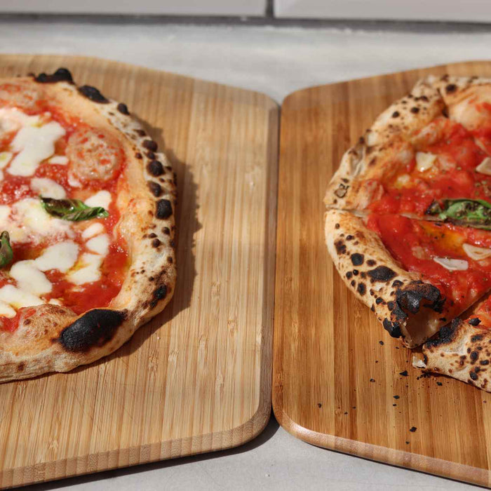 One cooked Margherita biga dough pizza with mozzarella, tomato sauce and basil on an Ooni Bamboo Peel & Serving Board next to a cooked marinara biga dough pizza with tomato sauce, garlic and basil on an Ooni Bamboo Peel & Serving Board.