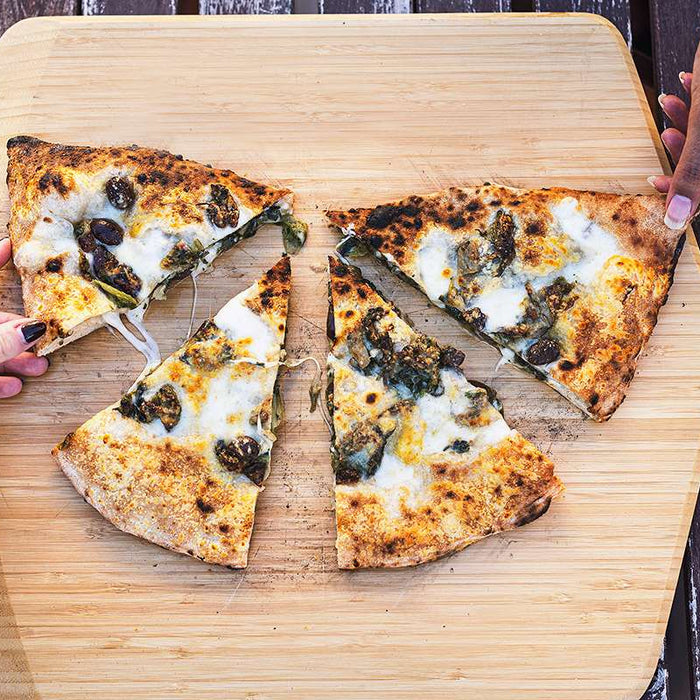 Two hands holding slices of cooked calzone with escarole and provola on top of an Ooni Bamboo Pizza Peel & Serving Board on a table.