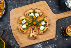 A pizza cut into a shape of a clover topped with pesto and ricotta on a wooden pizza peel