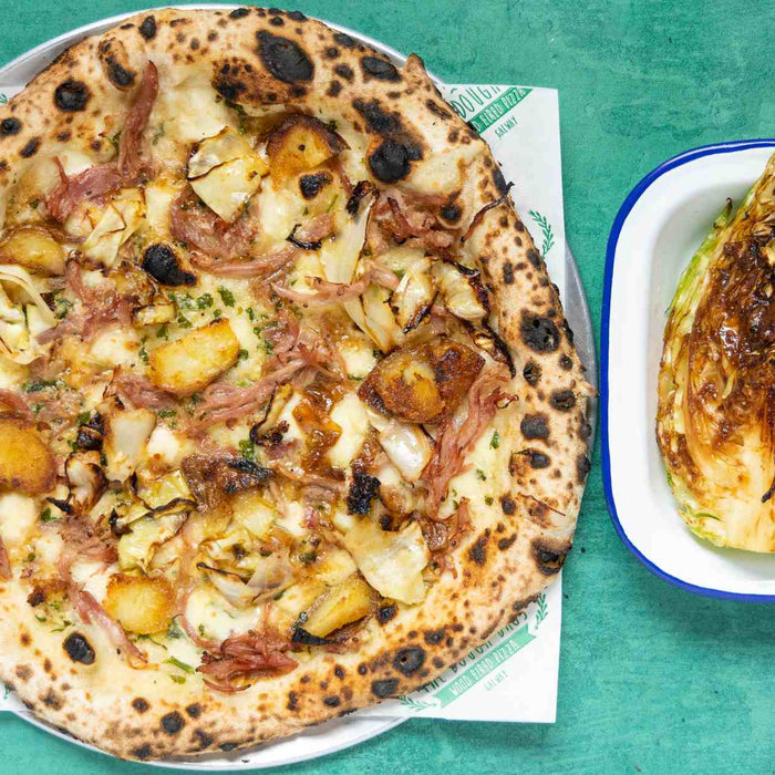 A pizza topped with ham, cabbage, potatoes with a side of braised miso cabbage
