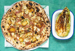 A pizza topped with ham, cabbage, potatoes with a side of braised miso cabbage