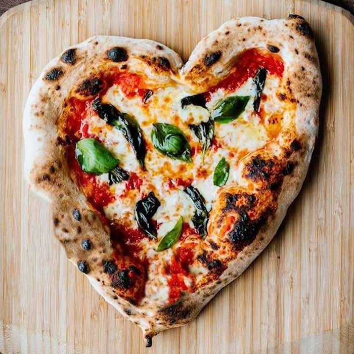 A heart shaped pizza topped with tomato, cheese and basil on a wooden pizza peel