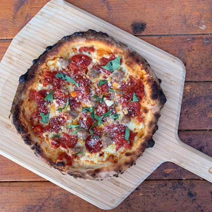 A thin crust pizza topped with tomato, cheese and basil on a wooden pizza peel. Baked using a Thin Crust Pizza Dough recipe.