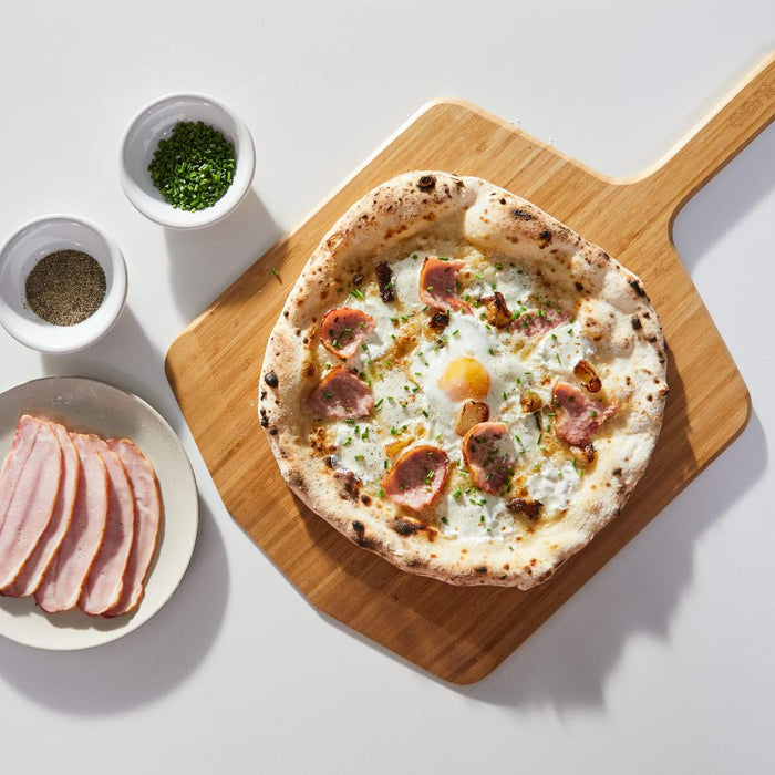 A wooden pizza peel with a pizza topped with cheese, egg and bacon