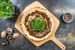 A pizza with mushroom ragu mince and rocket on top on a wooden pizza peel