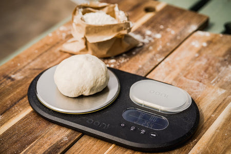 Ball of pizza dough on a set of scales, being used to measure pizza dough hydration.