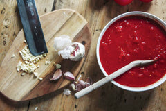 Classic Pizza Sauce in a bowl next to a wooden chopping board covered with crushed garlic. Made using a classic pizza sauce recipe.