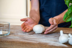 Ball of pizza dough being rolled out on a wooden chopping board, made using a Cold Proof Pizza Dough recipe.