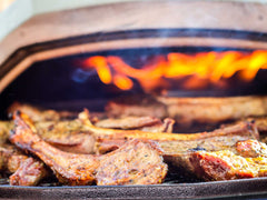 Lamb chops on a cast iron pan being grilled in an Ooni Karu 16 pizza oven