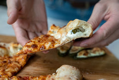 A slice of pizza with a jalapeno stuffed crust being held over a wooden pizza peel