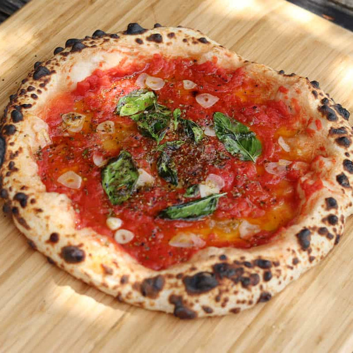 A pizza topped with tomatoes, basil and sliced garlic on a wooden pizza peel baked using a Marinara Pizza recipe