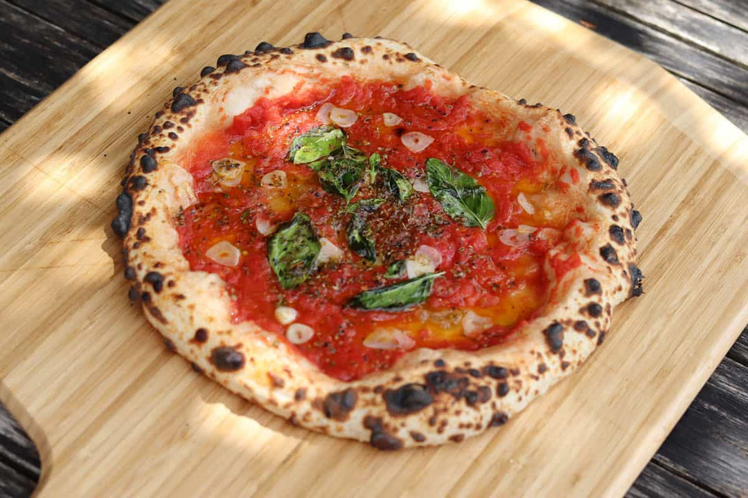 A pizza topped with tomatoes, basil and sliced garlic on a wooden pizza peel baked using a Marinara Pizza recipe