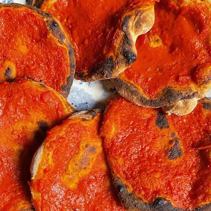 Hand holding a plate with six cooked pizzette rosse with tomato sauce.