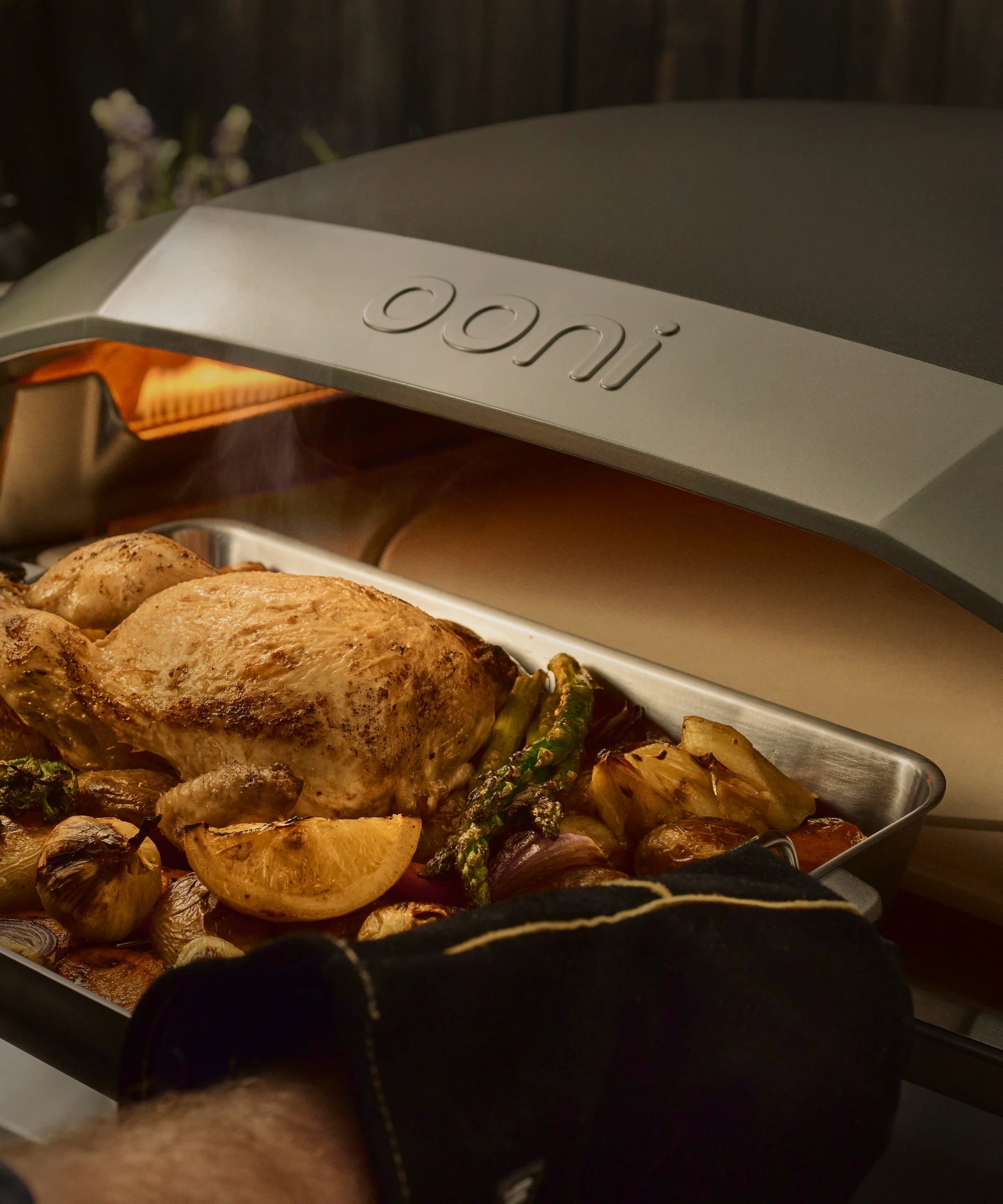 roasting pan with a whole chicken being removed from Koda 2 Max with rotating stone in use 