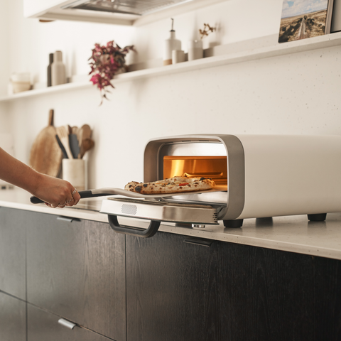 pizza being retrieved from ooni volt 2 electric pizza oven in polar white