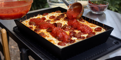 A laddle of sauce being poured on a cooked Detroit pizza 